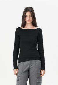 Top nero a maniche lunghe con scollatura ampia, texture liscia e design aderente, abbinato a pantaloni cargo grigi con tasche laterali.