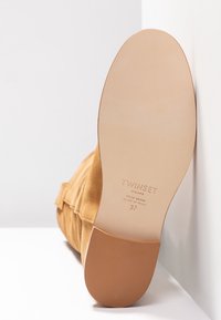 Bottine en daim marron clair reposant sur le côté, montrant une semelle en cuir propre avec le logo Twinset, taille 37, fabriquée en Italie.