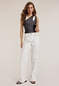Body asimmetrico nero con texture a rete, abbinato a jeans bianchi a gamba larga con dettagli a bottoni dorati e sandali neri con tacco.