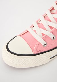 Roze platnena tenisica s bijelim vezicama, gumenim vrhom i crnim detaljima. Ima teksturiranu potplat i kružne metalne rupice za vezanje.