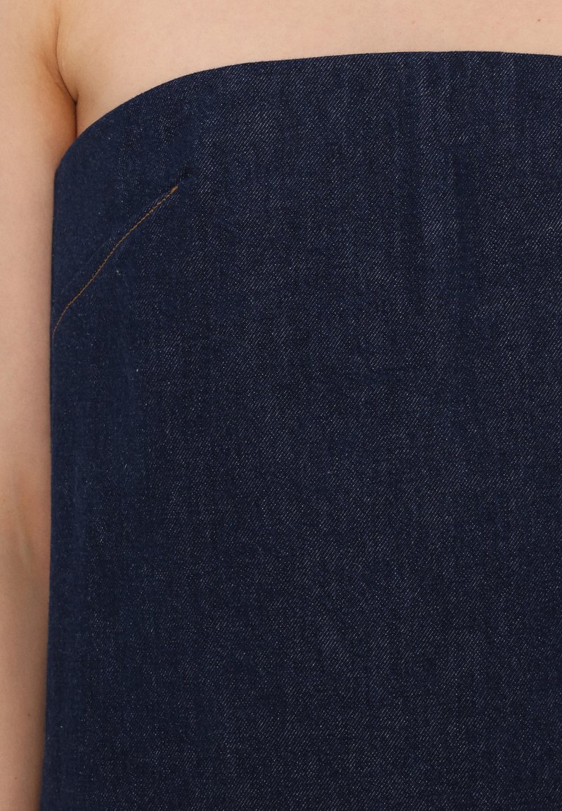 Donkerblauwe denimstof met een gladde textuur. Het strapless ontwerp heeft een subtiele stiksel detail aan de zijkant.