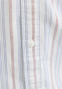 Tissu blanc avec des rayures verticales rouges et bleues, présentant un gros plan d'une patte de boutonnage sur une chemise.