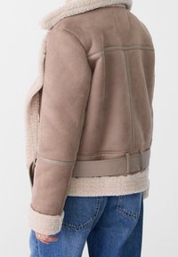 Bruine suède jas met een crèmekleurige shearling voering en manchetten, met een ceintuur in de taille en horizontale naaddetails op de achterkant.