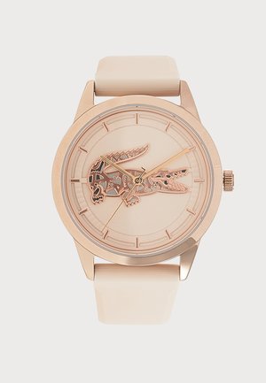 Montre ronde ton or avec bracelet beige et logo crocodile détaillé au centre du cadran.