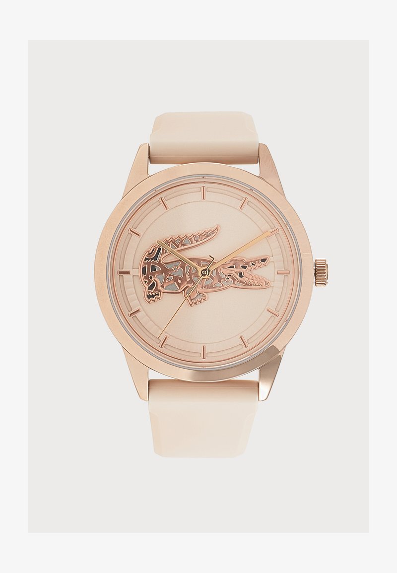 Montre ronde ton or avec bracelet beige et logo crocodile détaillé au centre du cadran.