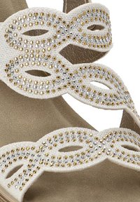 Sandal bianca con un design intrecciato decorato con strass argentati e dorati, abbinata a una suola beige soffice per un piacevole contrasto.