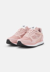 Zapatillas deportivas rosas con materiales de ante y malla, que presentan un talón blanco, suela de goma negra y un logotipo en el lateral y en la lengua.