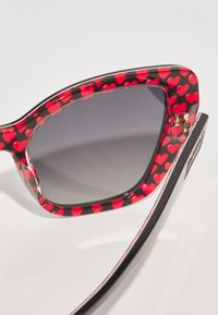 Oversized sunglasses with a black and red heart-patterned frame, gray lenses, and gold hardware accents on the hinges.