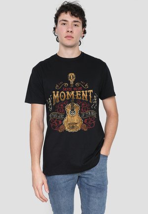 Schwarz Baumwoll-T-Shirt mit einem bunten Grafikdesign, das eine Gitarre, einen Schädel und den Text "NUTZE DEINEN MOMENT" zeigt. Kleidung mit kurzen Ärmeln und Rundhalsausschnitt.