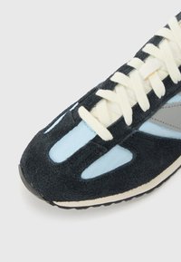 Chaussure de sport avec une tige en daim noir, des accents bleu clair, des lacets crème et une semelle en caoutchouc ; présente des découpes pour la respirabilité.