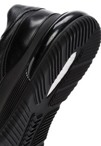 Scarpa da ginnastica nera con tomaia in pelle texturizzata, punta arrotondata e una spessa suola in gomma nera con un accento bianco e motivi di battistrada.