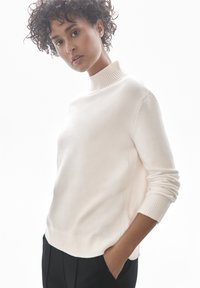 Crème-kleurige pullovertrui met een hoge, geribbelde halslijn, geribbelde manchetten en zijdetails. Zachte textuur, losse pasvorm en minimalistisch ontwerp.