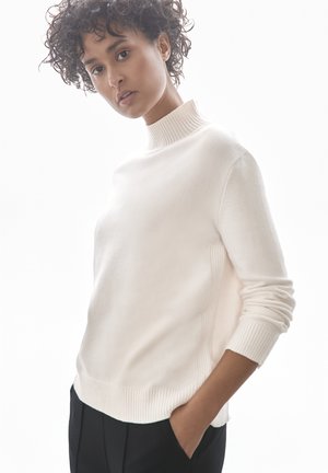 Pull en crème avec un col haut à côtes, des poignets à côtes et des détails sur les côtés. Texture douce, coupe ample et design minimaliste.