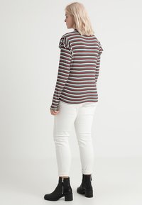 Stribet langærmet top i mørkerød, lys blå og hvid, med volanger på skuldrene. Sat sammen med hvide tætsiddende jeans og sorte ankelstøvler.