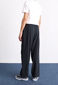 Svarta, löst sittande byxor i strukturerat tyg med elastisk midja och två sidofickor, kombinerade med en vit T-shirt med kort ärm och träningsskor.