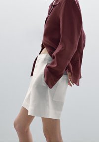 Witte shorts van lichtgewicht stof, gecombineerd met een losse, donkerrode blouse met lange mouwen. De blouse heeft een kraag en knoopdetails.