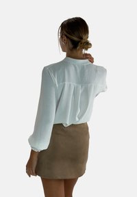 Leichtes, weißes langärmliges Bluse mit strukturiertem Finish und gerafften Manschetten, kombiniert mit einem kurzen, braunen Wildlederrock.