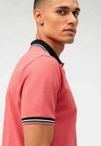 Polo rose en tissu texturé. Col marine rehaussé de rayures bleues et blanches. Manches courtes, coupe classique.