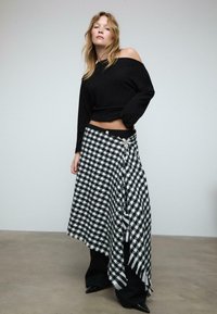 Crna dolčevita s otkrivenim ramenima u kombinaciji s dugom crno-bijelom kariranom suknjom koja se obavija oko tijela i ima resasti rub te dekorativne gumbe.