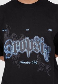 Sort bomulds t-shirt med et stort blåt grafisk design med teksten "Dropsize" og "Members Only" samt detaljerede engleillustrationer.