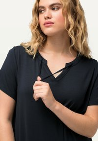 Czarny t-shirt z dekoltem w serek i krótkimi rękawami, wykonany z gładkiego materiału. Posiada detal w postaci sznurków przy dekolcie, umożliwiający regulację.