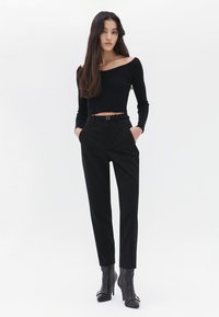 Schwarzes, geripptes Off-Shoulder-Top kombiniert mit maßgeschneiderten schwarzen Hosen, die über einen Gürtel und Schlitztaschen verfügen, abgerundet mit schwarzen Stiefeletten mit Absatz.