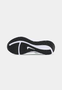 Black rubber outsole with a textured grip pattern, featuring a curved white midsole and a small green accent.