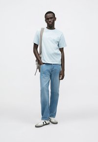 Jasnoniebieski t-shirt o luźnym kroju, zestawiony z jasnoniebieskimi dżinsami. Białe trampki z czarnymi paskami. Jasnoszara torba na ramię. Prosty design.