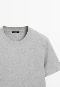 T-shirt gris clair à manches courtes et col rond en tissu doux, montrant la moitié supérieure avec étiquette de cou visible.