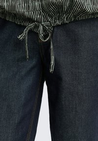 Dunkelblaue Jeans mit leichtem Struktur, verziert mit orangen Nähten und einem gestreiften, elastischen Bund in Schwarz und Weiß.