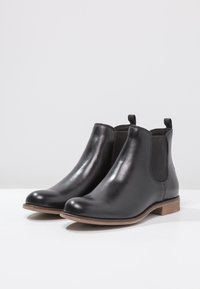 Schwarze Leder-Stiefeletten mit elastischen Seiteneinsätzen, abgerundeter Zehenpartie und niedrigem Holzabsatz. Glatte Textur mit glänzendem Finish.