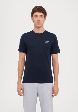 T-shirt en coton bleu marine à manches courtes, col rond, avec un petit logo blanc sur la poitrine gauche. Texture lisse, design ajusté.