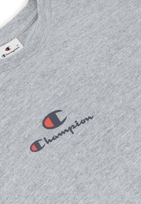 Grijze T-shirt met korte mouwen van lichtgewicht stof. Voorzien van een zwart en rood Champion-logo op de voorkant. Klassiek ontwerp met ronde hals.