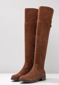 Brązowe zamszowe kozaki za kolano o gładkiej, miękkiej fakturze, wyposażone w boczny zamek i niski obcas typu blok dla stabilności.