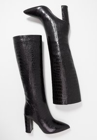 Sorte knæhøje støvler med en blank krokodilletekstur, spids snude og chunky hæl. Det slanke design fremhæver det skinnende materiale og formen.