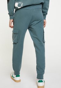 Teal sweatpants voor heren met zijcargo zakken, elastische tailleband en geribde manchetten. Gemaakt van een zachte stof, met een minimalistisch ontwerp.