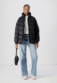 Casaco puffer preto com gola alta, combinado com um suéter de ponto creme e jeans de perna larga azul claro. Os acessórios incluem uma pequena bolsa preta.