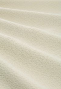 Texturiertes cremefarbenes Gewebe, das ein subtil geometrisches Muster zeigt. Die Oberfläche hat sanfte Falten, was Flexibilität und eine glatte Haptik anzeigt.