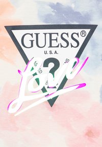 T-shirt graphique avec un fond tie-dye pastel, un logo triangle noir avec "GUESS®" et un texte "Love" brillant et multicolore superposé.