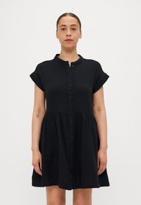 Rochie neagră cu nasturi, cu guler rotund, mâneci scurte și talie strânsă. Fabricată dintr-un material ușor, cu o textură netedă.
