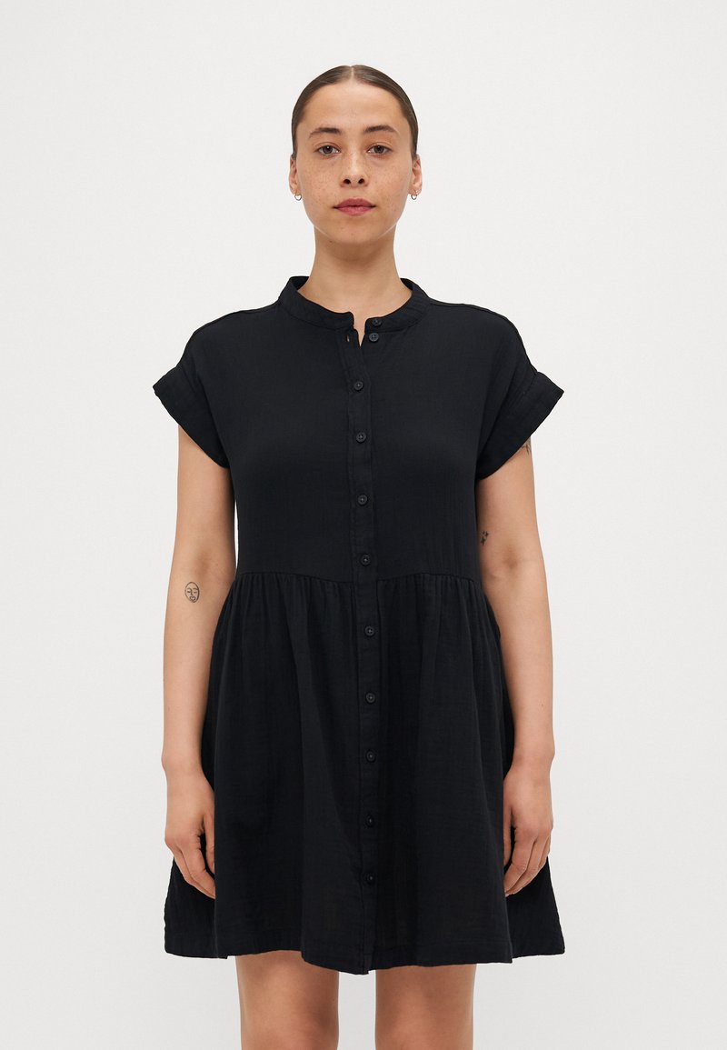 Rochie neagră cu nasturi, cu guler rotund, mâneci scurte și talie strânsă. Fabricată dintr-un material ușor, cu o textură netedă.