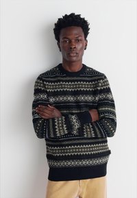 Gestickter Pullover mit dunklem Hintergrund, der grüne und beige geometrische Muster zeigt. Rippbündchen und Saum; Rundhalsausschnitt-Design.