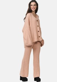 Stickad tvådelad outfit i mjuk blushrosa. Tröjan har en V-ringning och stora knappar, och är i kombination med vida, texturerade byxor.