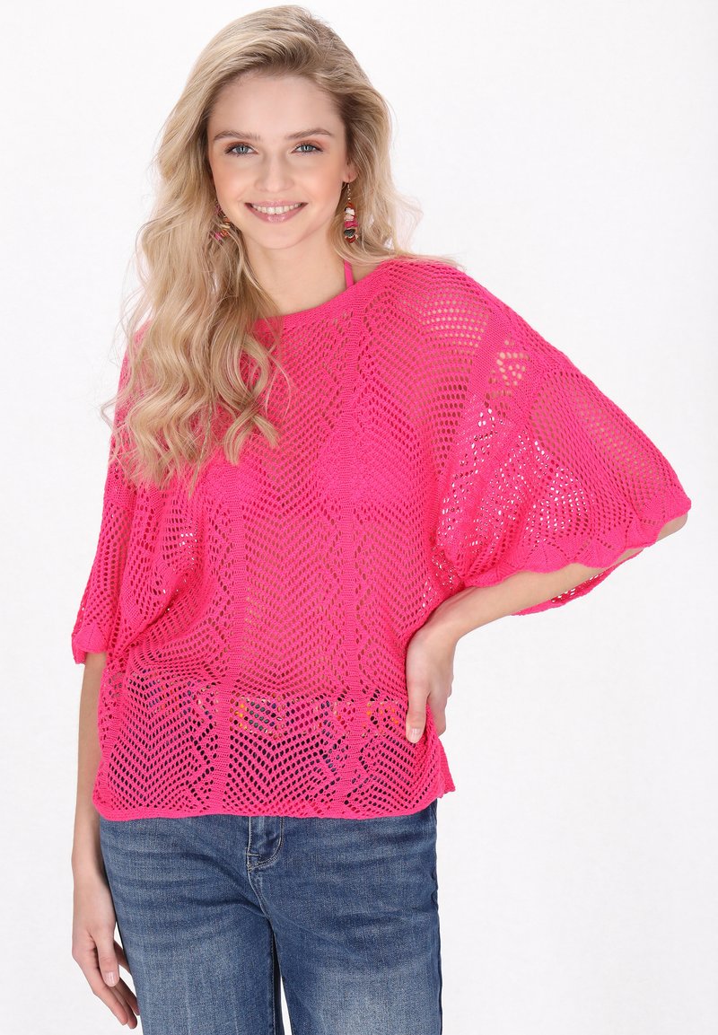 Helles pink gestricktes Sweatshirt mit lockerer Passform, das ein rautenförmiges Netzmuster und kurze Dolmanärmel aufweist. Kombiniert mit Jeans.