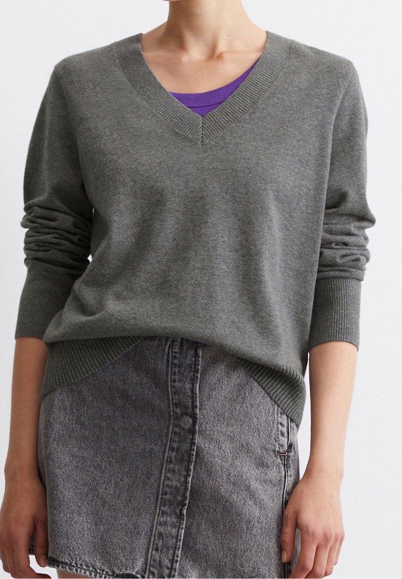 Harmaa V-pääntie neulepaita pehmeästä langasta, jossa on ribattu hihansuu ja helma. Päällä violetti toppi ja parina musta farkkuhame.