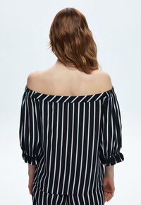 Sort og hvid stribet off-the-shoulder top med trekvartærmer og flæse detaljer ved manchetterne. Glat stofstruktur.