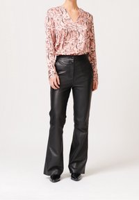 Blusa a maniche lunghe rosa con motivo astratto marrone abbinata a pantaloni in pelle nera a zampa d'elefante, con chiusura frontale a bottoni e texture liscia.
