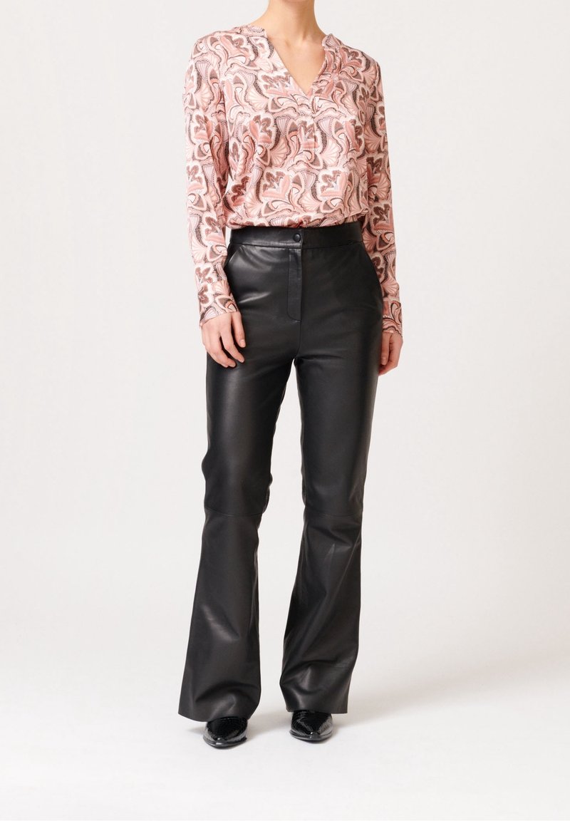 Blusa a maniche lunghe rosa con motivo astratto marrone abbinata a pantaloni in pelle nera a zampa d'elefante, con chiusura frontale a bottoni e texture liscia.