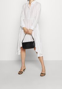 Abito bianco a righe con colletto e chiusura a bottoni, abbinato a una borsa nera con texture e sandali aperti a punta leopardati.