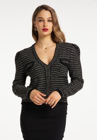 Svart och vit texturerad cardigan med puffiga axlar, v-ringning och framknappar. Bärs över en figurnära svart kjol.